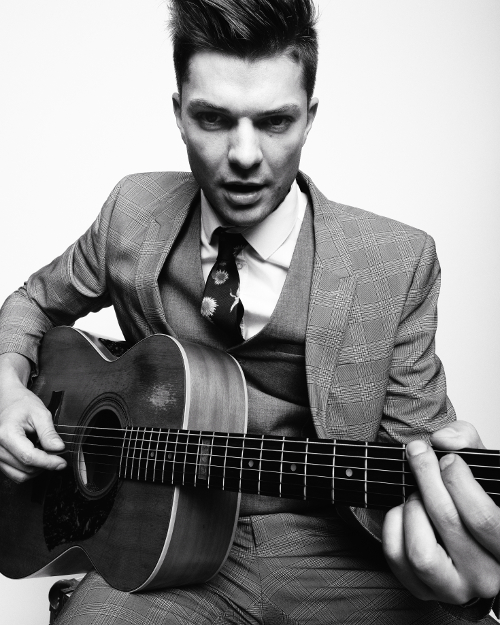 Unique black and white portrait photo with light background of man sitting and posing playing a guitar. Unique black and white portrait photo with light background of man sitting and posing playing a guitar.